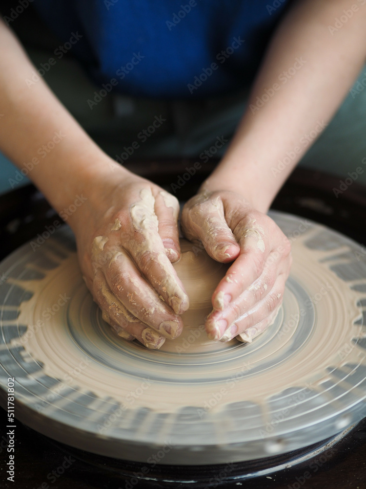 Young female master working on a potter’s wheel, creates clay dishes. Ceramist young woman making clay product on pottery lathe in studio, workshop, top view. Small business, hobby, ceramic concept.