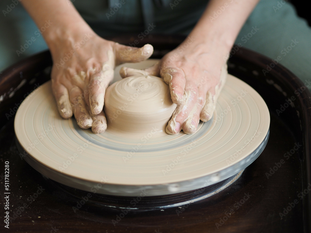 Young female master working on a potter’s wheel, creates clay dishes. Ceramist young woman making clay product on pottery lathe in her studio, workshop top view. Young female master working on a potter’s wheel, creates clay dishes. Ceramist young woman making clay product on pottery lathe in her studio, workshop top view.