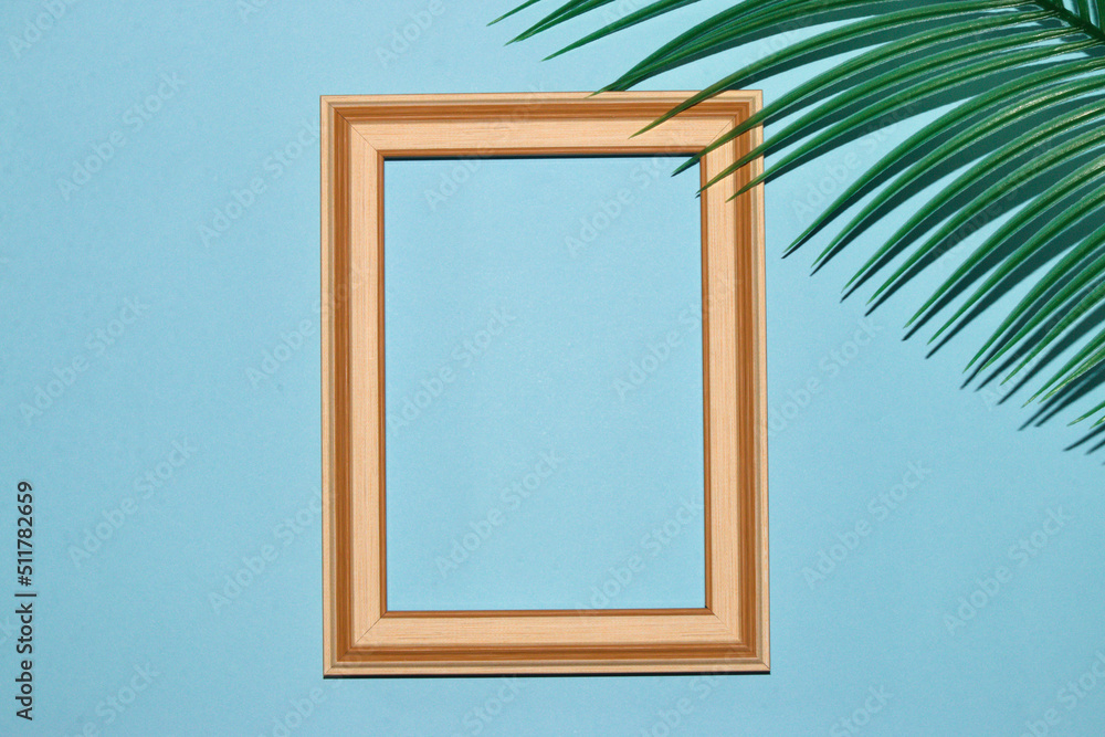 wooden frame on pastel blue background as copy space in the corner of palm leaf background, creative summer design, tropical background wooden frame on pastel blue background as copy space in the corner of palm leaf background, creative summer design, tropical background