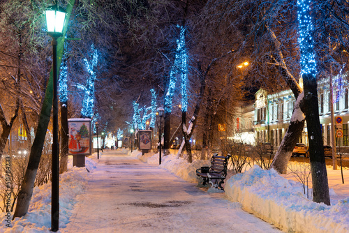 Evening winter alley with benches and New Year's decorations.