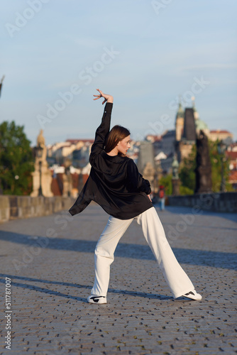 Young woman in casual stylish clothes dancing on the stone bridge of old town in a Prague. Active lifestyle and dancing concept.