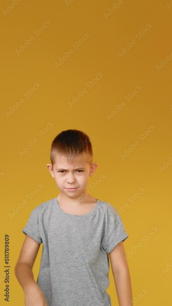 Disappointed child. Dislike gesture. Bad idea. Refusal signal. Vertical portrait of dissatisfied skeptic boy showing thumb down stop nope disapproval sign isolated on yellow copy space background. Disappointed child. Dislike gesture. Bad idea. Refusal signal. Vertical portrait of dissatisfied skeptic boy showing thumb down stop nope disapproval sign isolated on yellow copy space background.