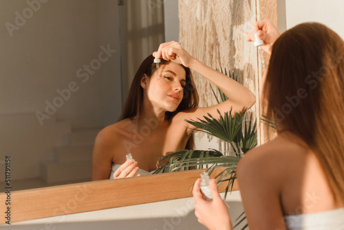 A beautiful young woman uses a moisturizing anti-aging facial serum in the bathroom. Body skin care and cosmetic application concept