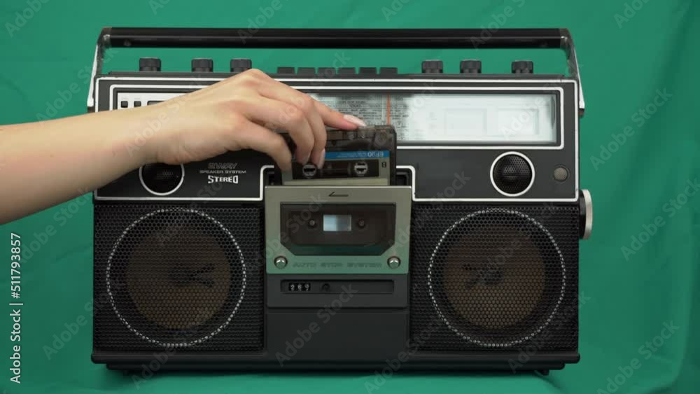 Girl puts vintage cassettes into a black radio tape recorder on a green