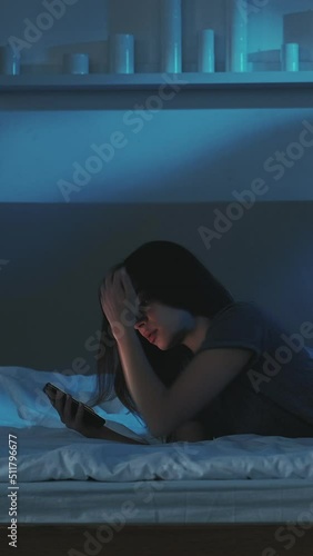 Insomnia woman. Social media addiction. Virtual life. Pretty surprised lady laying at bed scrolling smartphone in light shadow room interior. Vertical video.