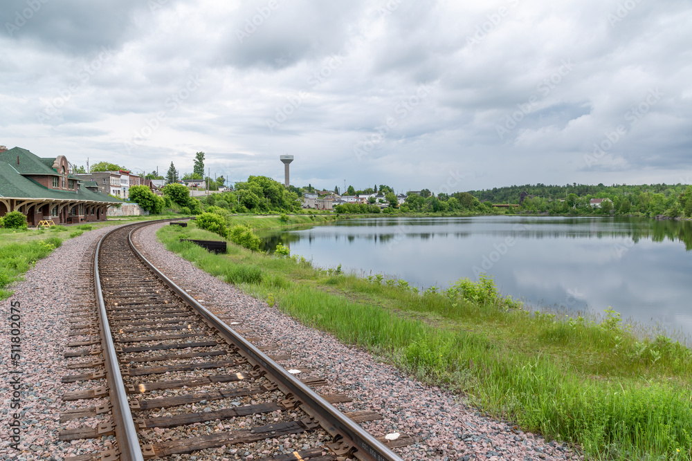 A railway track curves its way around a small lake up to the station in the small former mining town of Cobalt, Ontario on a gloomy day.