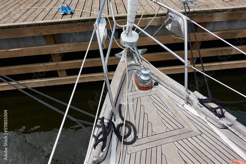 An elegant two masted sailboat (ketch) moored to a pier in a yacht marina. Wooden teak deck, rigging equipment, mast winch, ropes. Transportation, cruise, vacations, service and repair themes