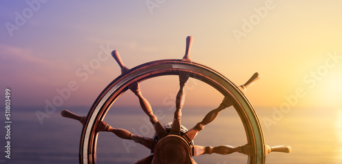 Ship steering wheel, commonly known as helm, with the ocean at sunset in the background. 3D Rendering, illustration photo