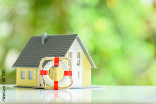 Property and home insurance, financial concept : Red lifebuoy and a blurred model house on a table, depicting policies that cover destruction and damage to a residence's interior and exterior.