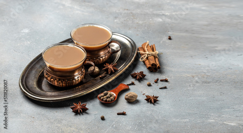 Indian masala chai tea. Hot masala chai spiced tea with milk and spices is poured into a glass glass on gray background. Long banner format. place for text