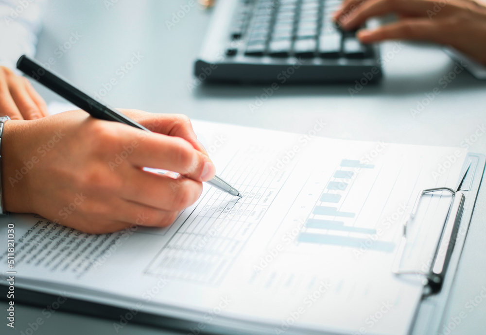Unrecognizable business person analyzing graphs and taking notes Unrecognizable business person analyzing graphs and taking notes