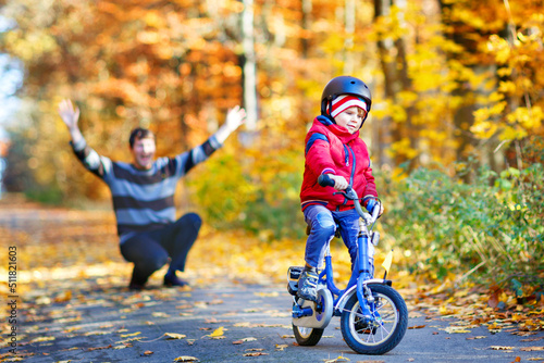 Little kid boy learning moving on bicycle. His father teaching his son biking. Happy man and child. Active family leisure. Child with helmet on bike. Safety, sports, leisure with kids concept.