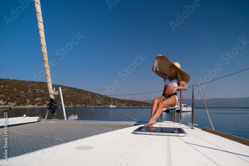 Beautiful young blond woman in bikini sitting on catamaran bow at sunny summer day