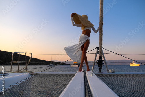 Beautiful young blond woman in a dress standing on yacht stern on the sea or ocean at sunset