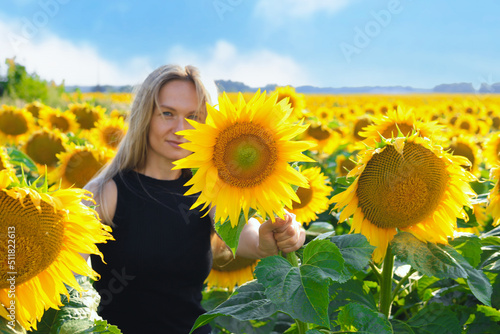 Beautiful blonde woman in black dress enjoying nature . Happy smiling female standing in sunflowers field.
