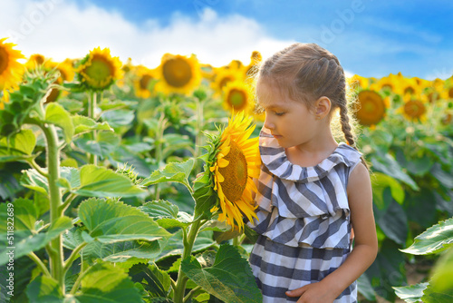 Beautiful little girl enjoying nature . Happy smiling female kid standing in sunflowers field.