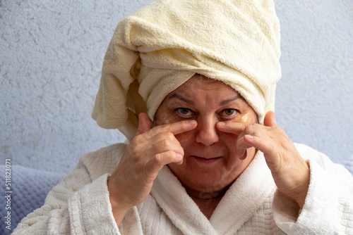 Older woman holds patches glued to her face with her fingers. Selective focus. A picture for articles about age-related facial care.