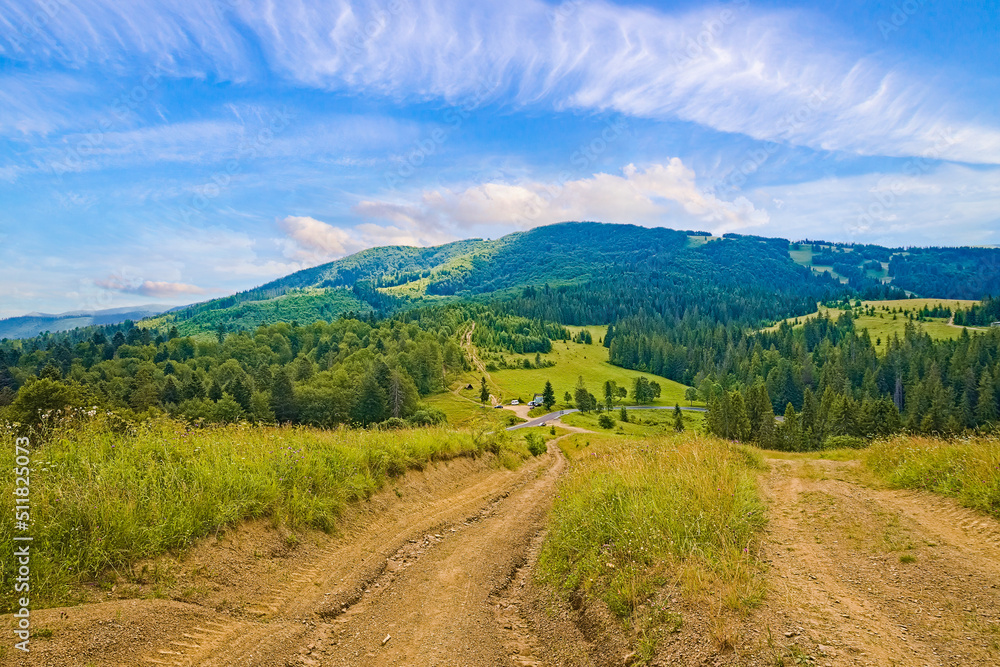 Beautiful field with dirt road and forest, covered with hills behind the mountain and the sky with barns. landscape background.
