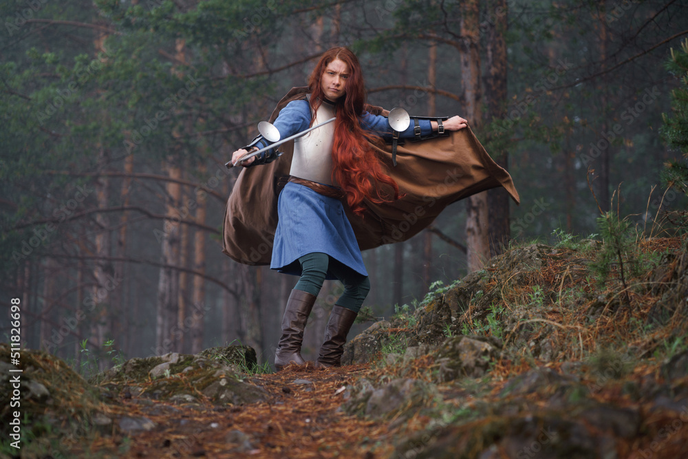 Fototapeta premium Young red-haired girl in medieval knight's armor in summer forest