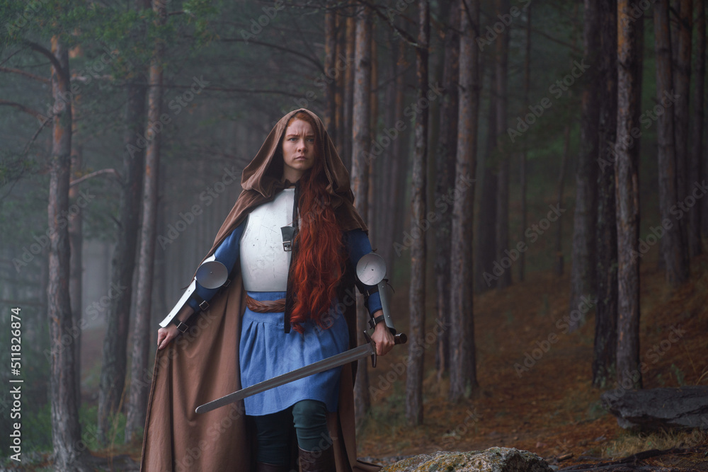 Fototapeta premium Red-haired girl in armor and raincoat in forest. Historical concept