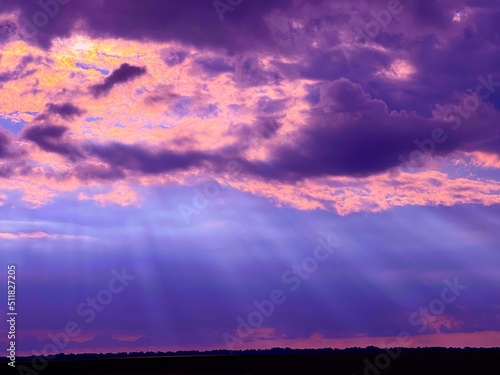 Blue sun rays and sunset clouds. Dramatic sky with stormy clouds over dark land at evening.