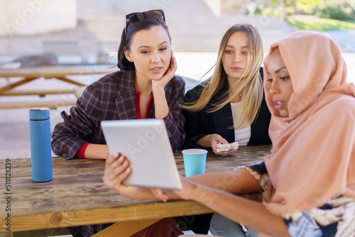 Cheerful diverse women sharing tablet during coffee break in cafe