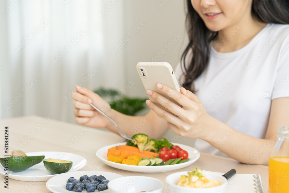 Dieting, asian young woman eating, holding fork at broccoli, diet plan nutrition with fresh vegetables salad, enjoy meal while using smartphone. Nutritionist of healthy, nutrition of weight loss. Dieting, asian young woman eating, holding fork at broccoli, diet plan nutrition with fresh vegetables salad, enjoy meal while using smartphone. Nutritionist of healthy, nutrition of weight loss.