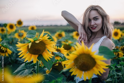 A young slender beautiful girl in a T-shirt in a field of sunflowers at sunset