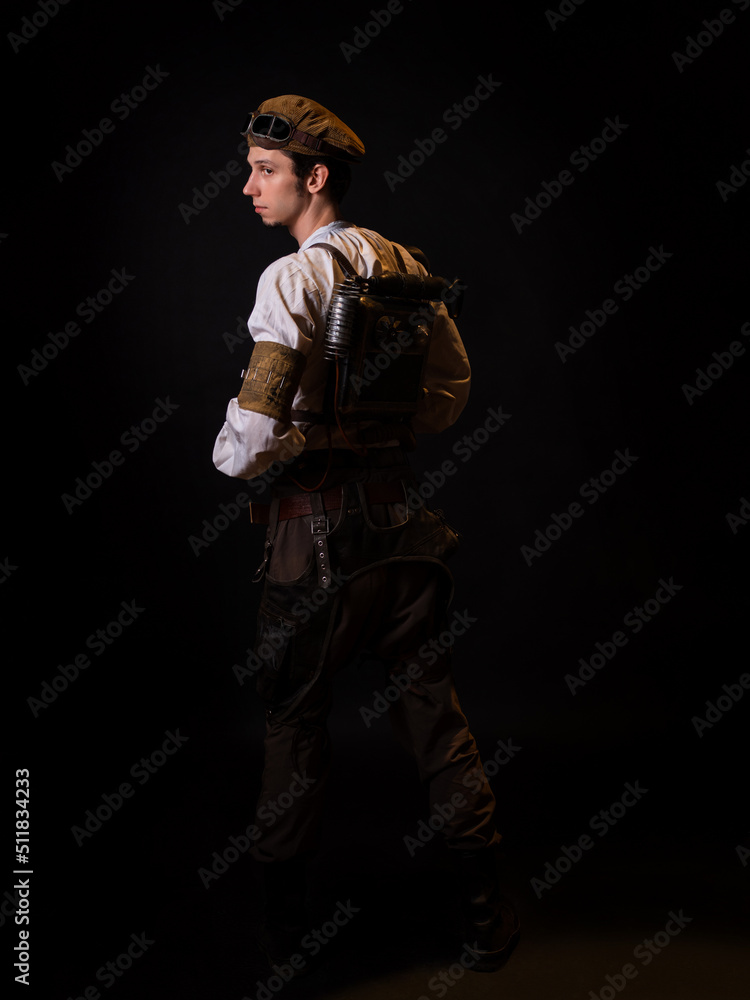 Fototapeta premium A guy in a steampunk image, a pilot or a mechanic. Retro style, fantastic image. portrait on black. Fantastic steam satchel behind back