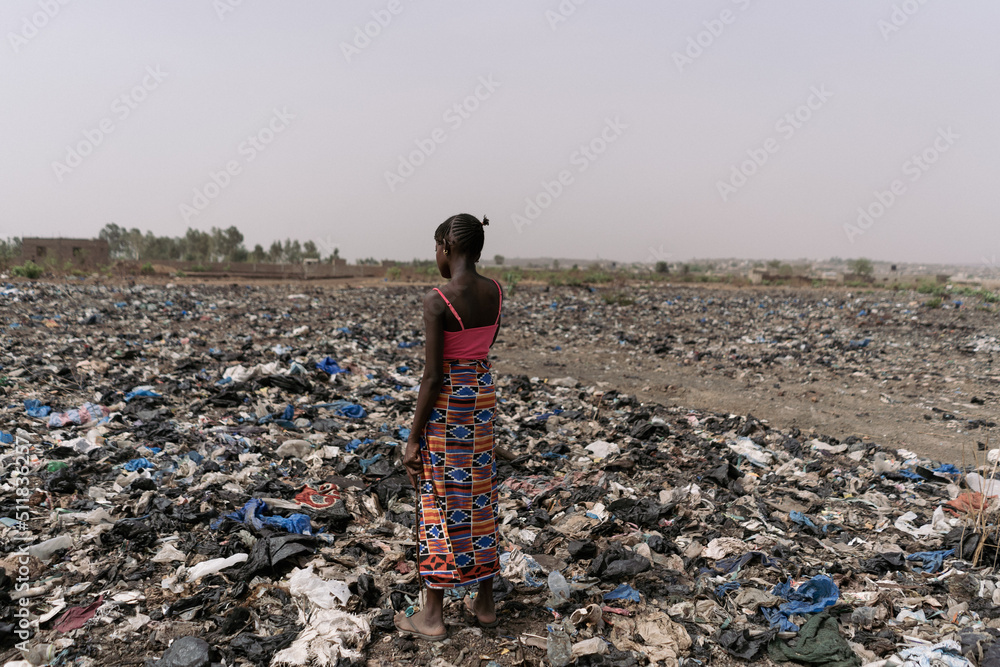 Lonely little African girl standing on a landfill in the midst of all types of garbage; environmental pollution concept