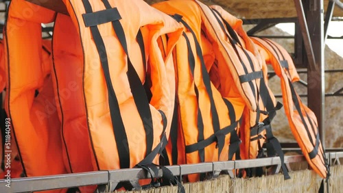 Orange life jackets in store by the sea. Many life jackets hang in a row on hangers. Protective safety clothing at rental boat store.