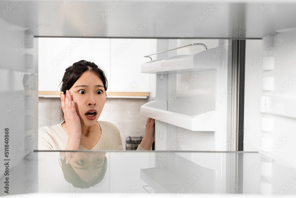 Shocked asian woman looking inside empty fridge Shocked asian woman looking inside empty fridge