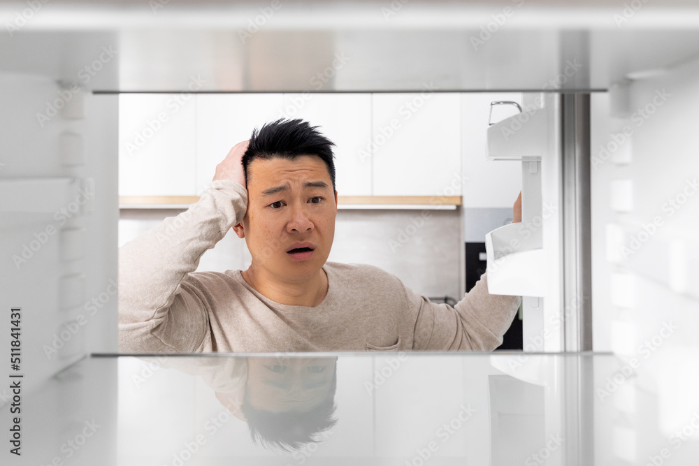 Shocked chinese man looking inside empty fridge