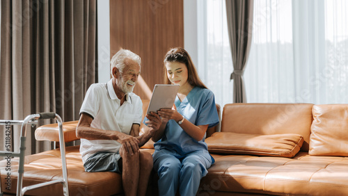 Fotografering Asian nurse and senior man looking medical record on digital tablet at home