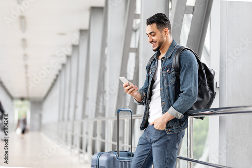 Obraz na plátně Smiling Arab Male Traveller With Smartphone And Luggage Waiting In Airport