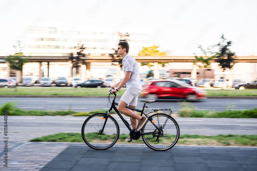 Obraz premium Young modern man riding bicycle on city streets, motion blur, panning shot, summer time