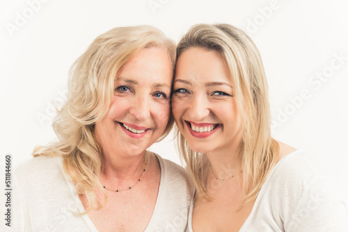 Blonde european good-looking women in their 30s wearing white outfits looking at camera, leaning their heads close to each other. Studio shot. High quality photo