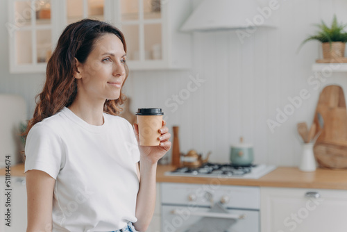 Relaxed smiling woman with paper cup of coffee at home. Girl at kitchen in morning.