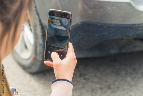 Outdoor shot of an unrecongnizable caucasian woman taking a photo on a road of her cars front fender with a modern smartphone. High quality photo