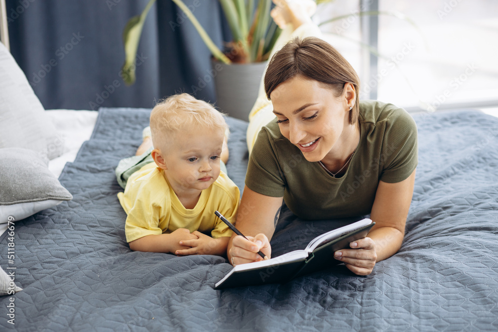 Mother with her little son reading a book on the bed Mother with her little son reading a book on the bed