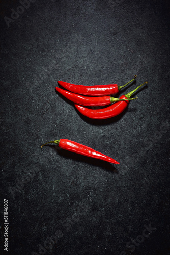 Red chilli peppers over dark background. Top down shot of glossy vegetable reflecting light. Spicy ingredients in kitchen