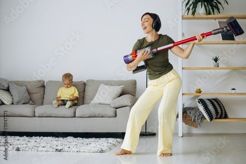 Woman vacuuming the house while little son sitting on sofa