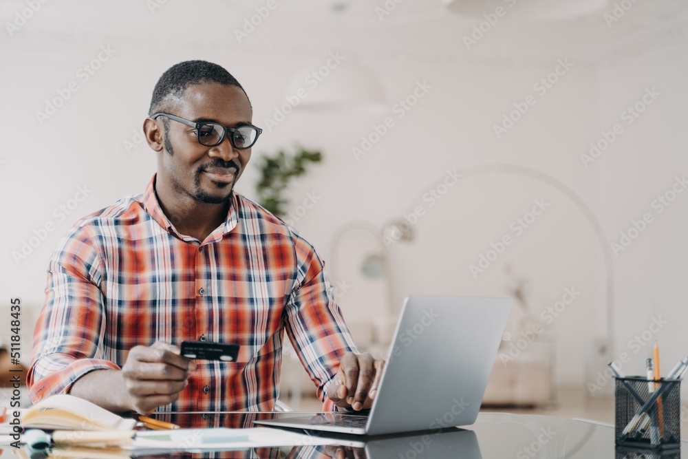 Happy african american man in glasses is purchasing online using laptop and credit card. Happy african american man in glasses is purchasing online using laptop and credit card.