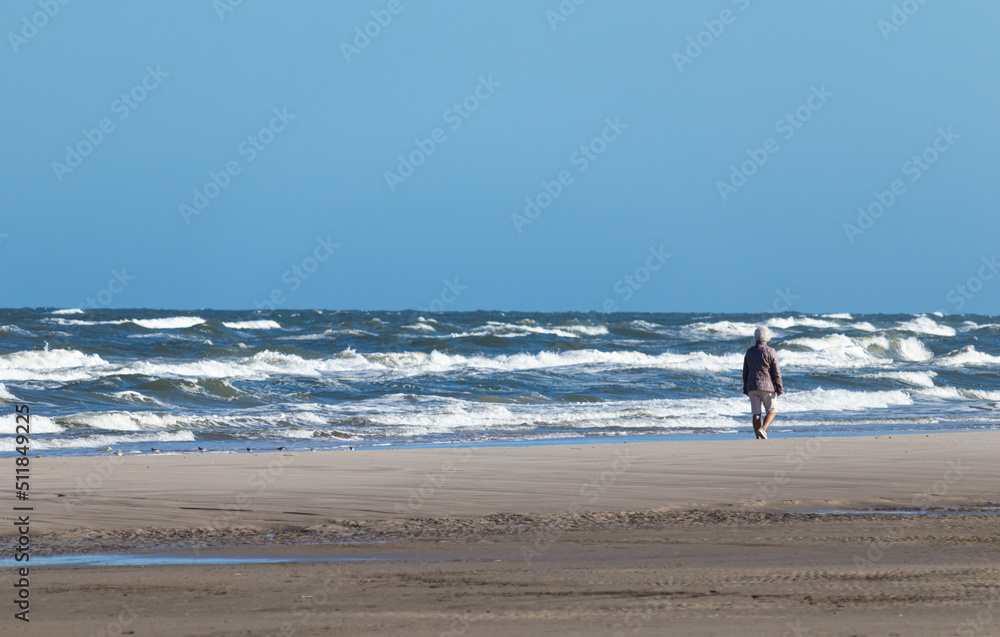 woman walking on beach at wavy ocean