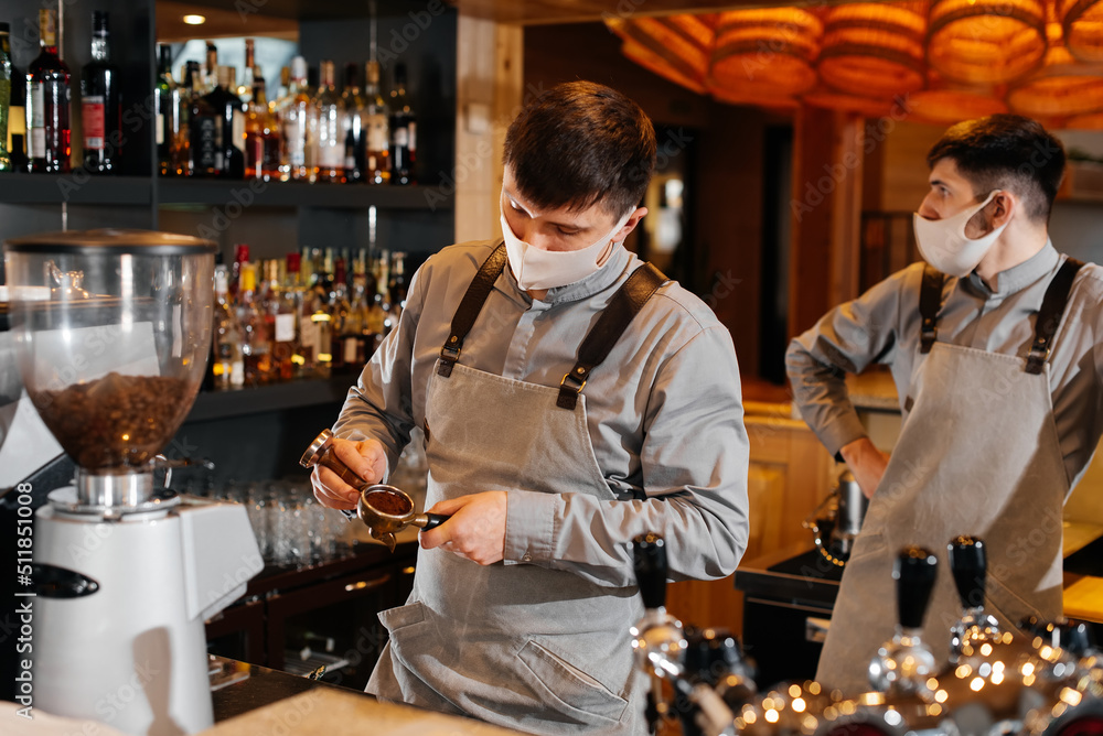 Two masked baristas prepare exquisite delicious coffee at the bar in the coffee shop. The work of restaurants and cafes during the pandemic.