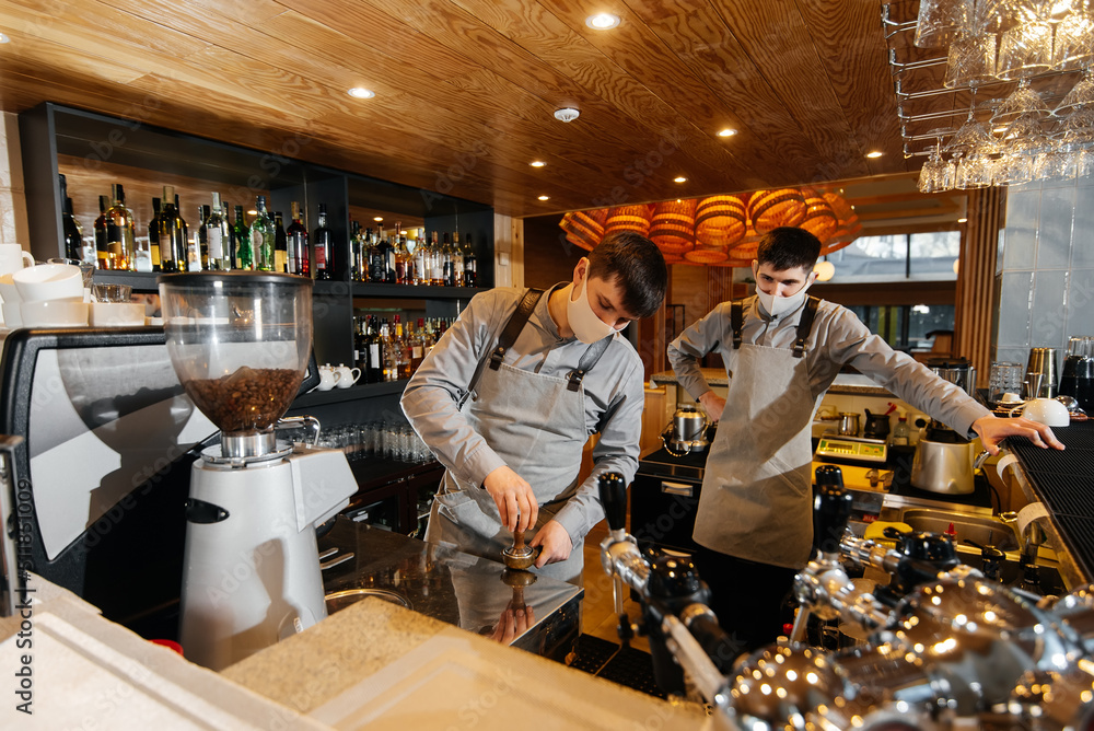 Two masked baristas prepare exquisite delicious coffee at the bar in the coffee shop. The work of restaurants and cafes during the pandemic.