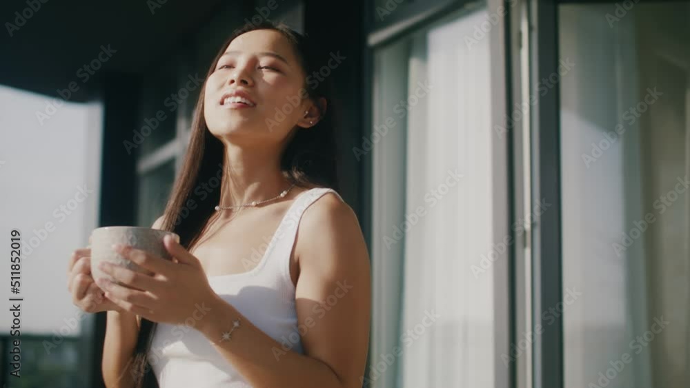 Attractive young woman drinking coffee holding cup standing on balcony with beautiful scenery sunsets outdoors. Asian happy smiling female. Slow motion. Attractive young woman drinking coffee holding cup standing on balcony with beautiful scenery sunsets outdoors. Asian happy smiling female. Slow motion.