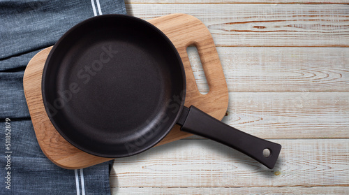 Black fry pan and board with napkin on wooden table. Top view mockup