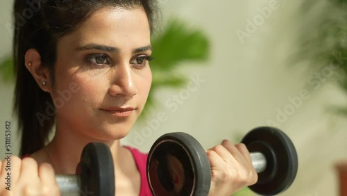 Closeup shot of Young Indian woman doing arm workout with dumbbells in living room.Sport and fitness.Asian female doing exercise with dubbell at home gym.healthy concept. photo