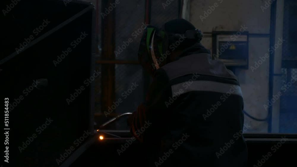 Welder welds large trailer frame at a factory. Employee of a factory for welding parts is actively working to pass the shift. Welder welds large trailer frame at a factory. Employee of a factory for welding parts is actively working to pass the shift.